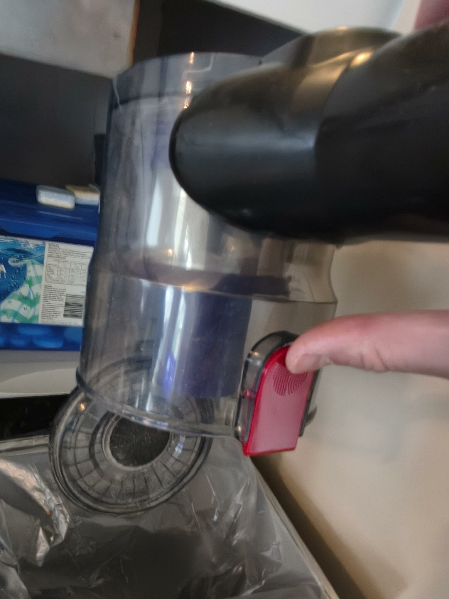 Staubbehälter über dem Mülleimer leeren – roter Entriegelungsknopf öffnet die Bodenklappe